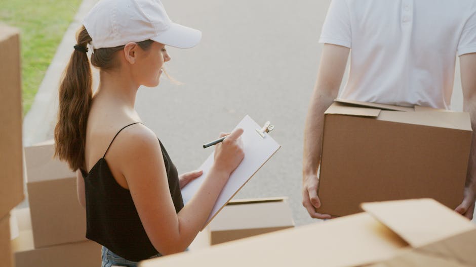 A woman with long brown hair tied in a ponytail, wearing a white cap and a black sleeveless top, is outdoors in a driveway or parking area during daytime, writing on a clipboard with a pen while surro